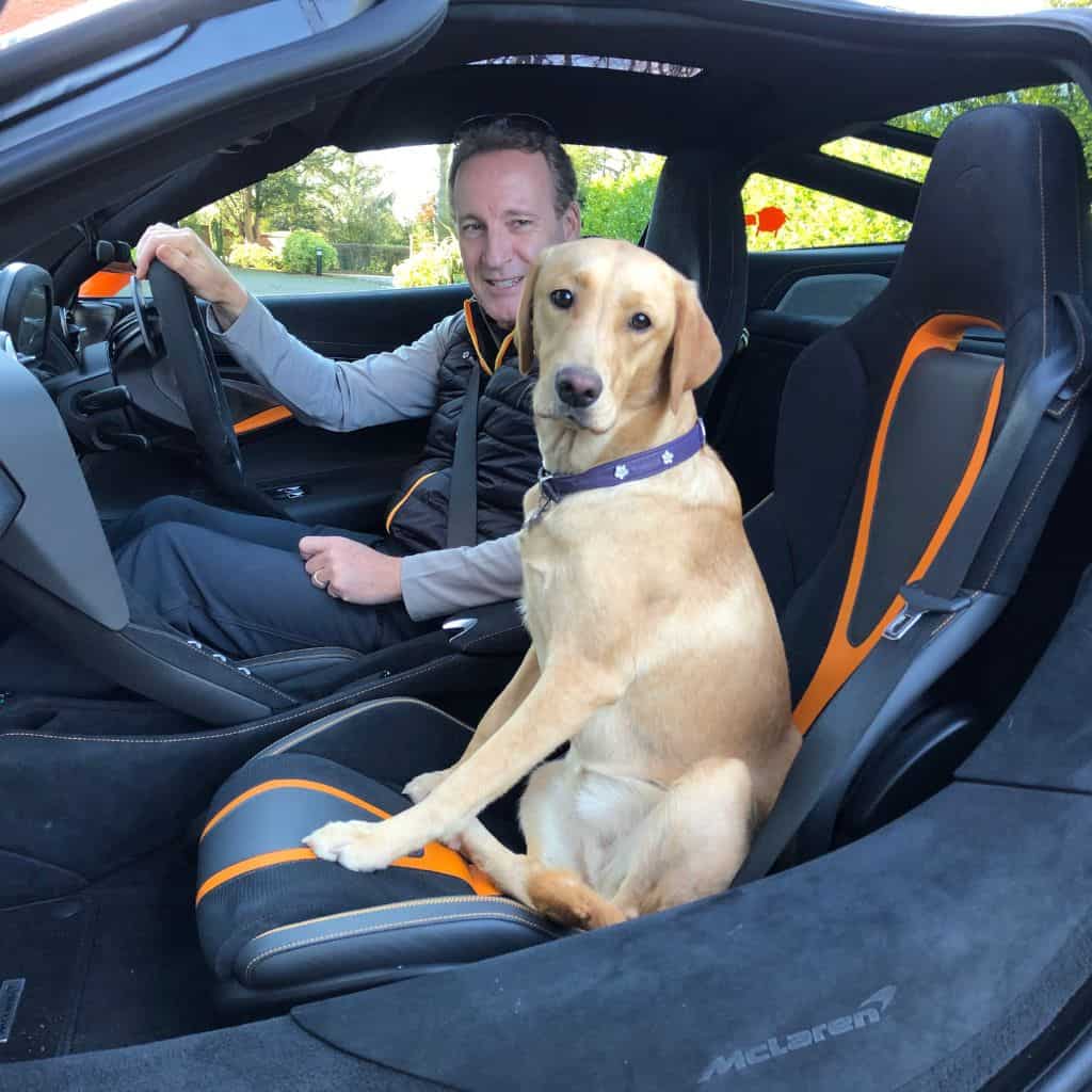 Wayne of waynes world of wheels sitting in a McLaren 720s car with a fox red labrador in the passenger seat