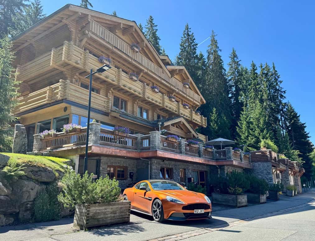Richard Bransons Lodge in Verbier with an Orange Aston Martin DBS parked in front of it while on the Wwow Bransons Blitz Alpine Tour