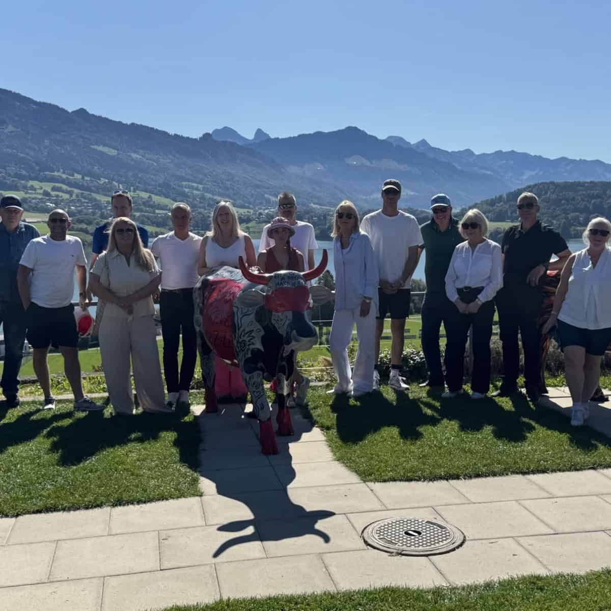 group of men and women who are members of Waynes World Of Wheel standing together in front of the Swiss Alps on a very sunny summers day